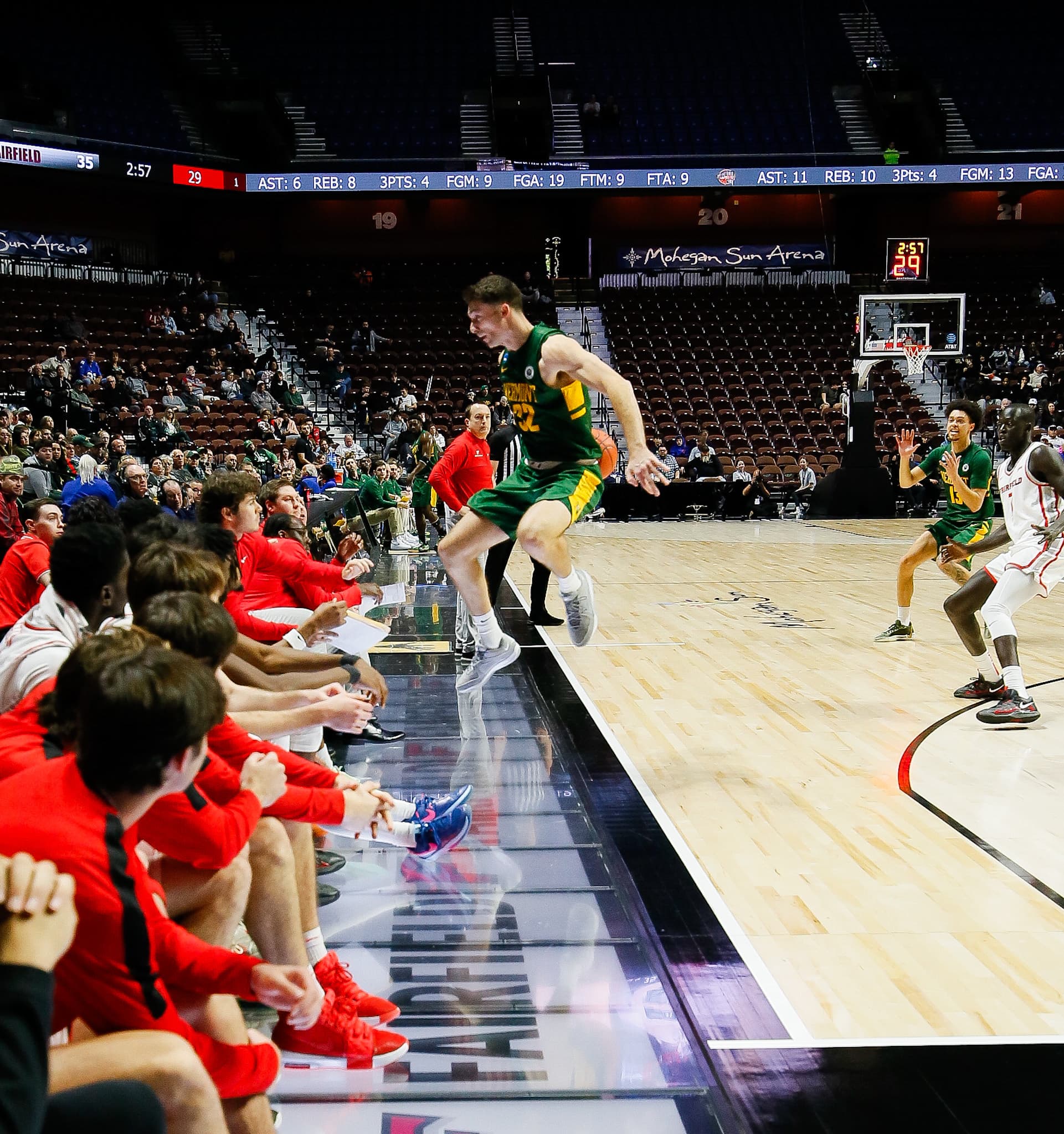 Vermont player landing on a Courtside display panel along the sideline beside the Fairfield bench