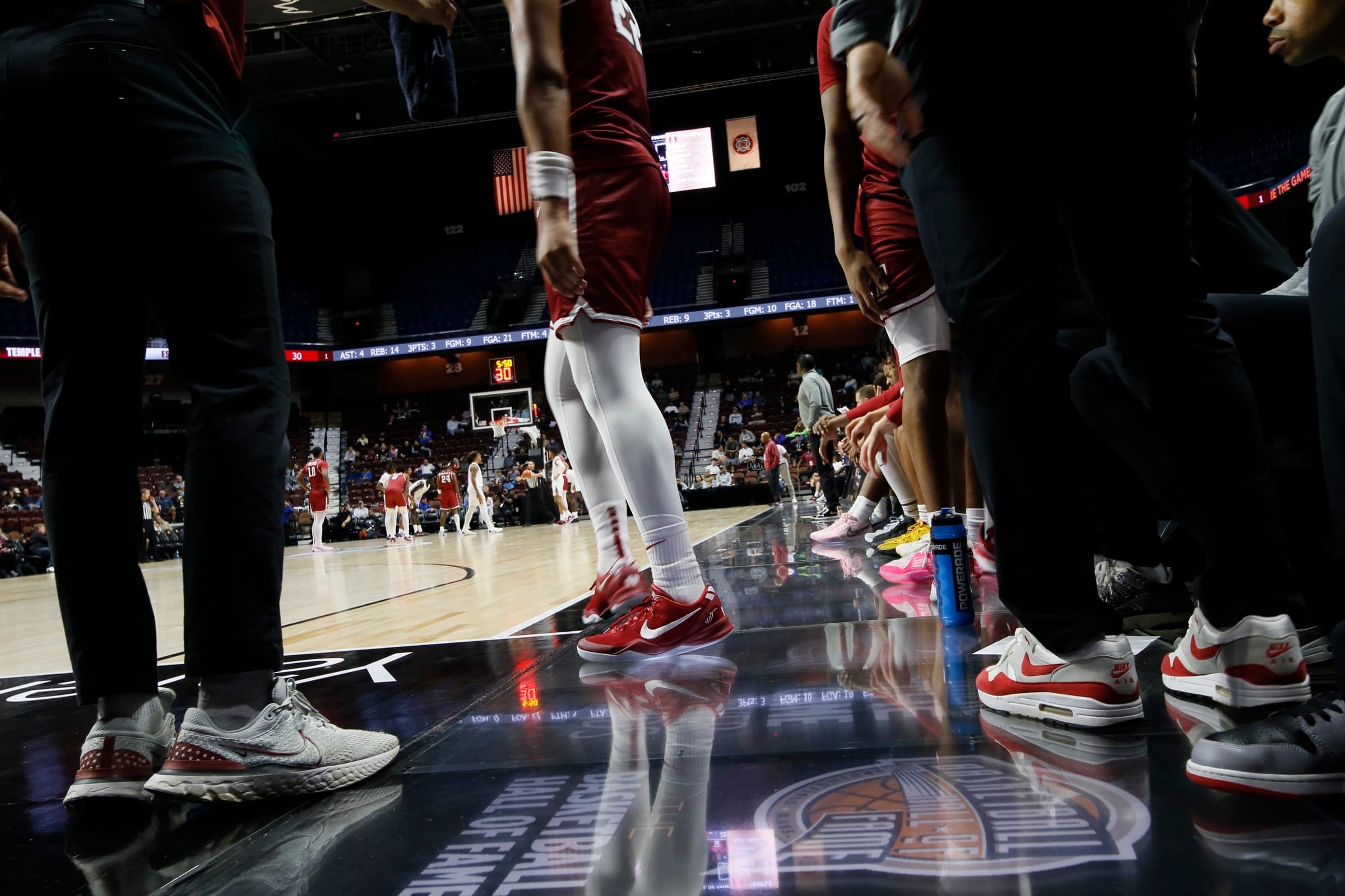 Players' red sneakers on the glossy Basketball Hall of Fame sideline panels as a game plays on in the arena