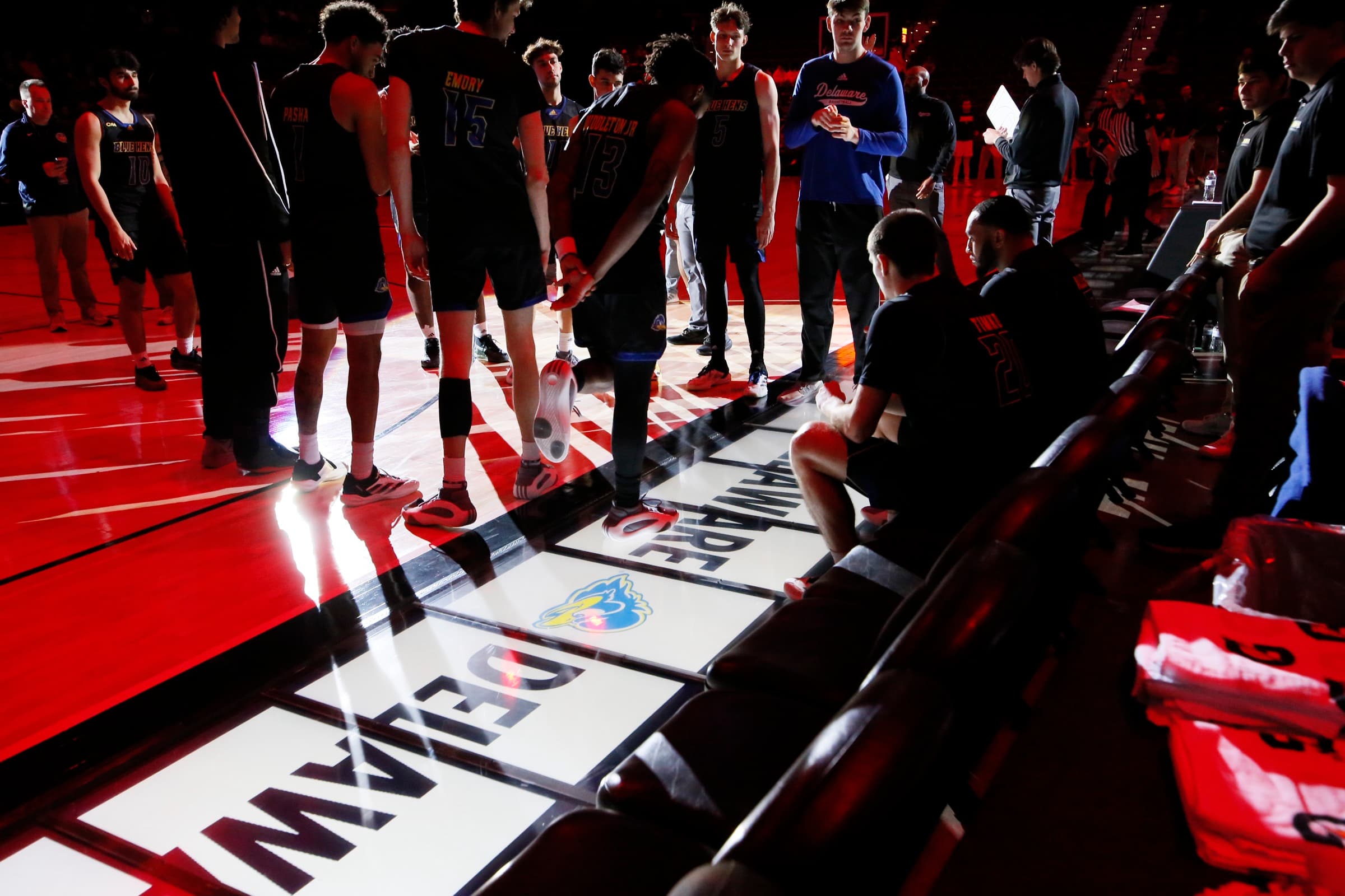 Delaware players huddled on court beside the bench, above lit Courtside floor panels showing the Delaware logo