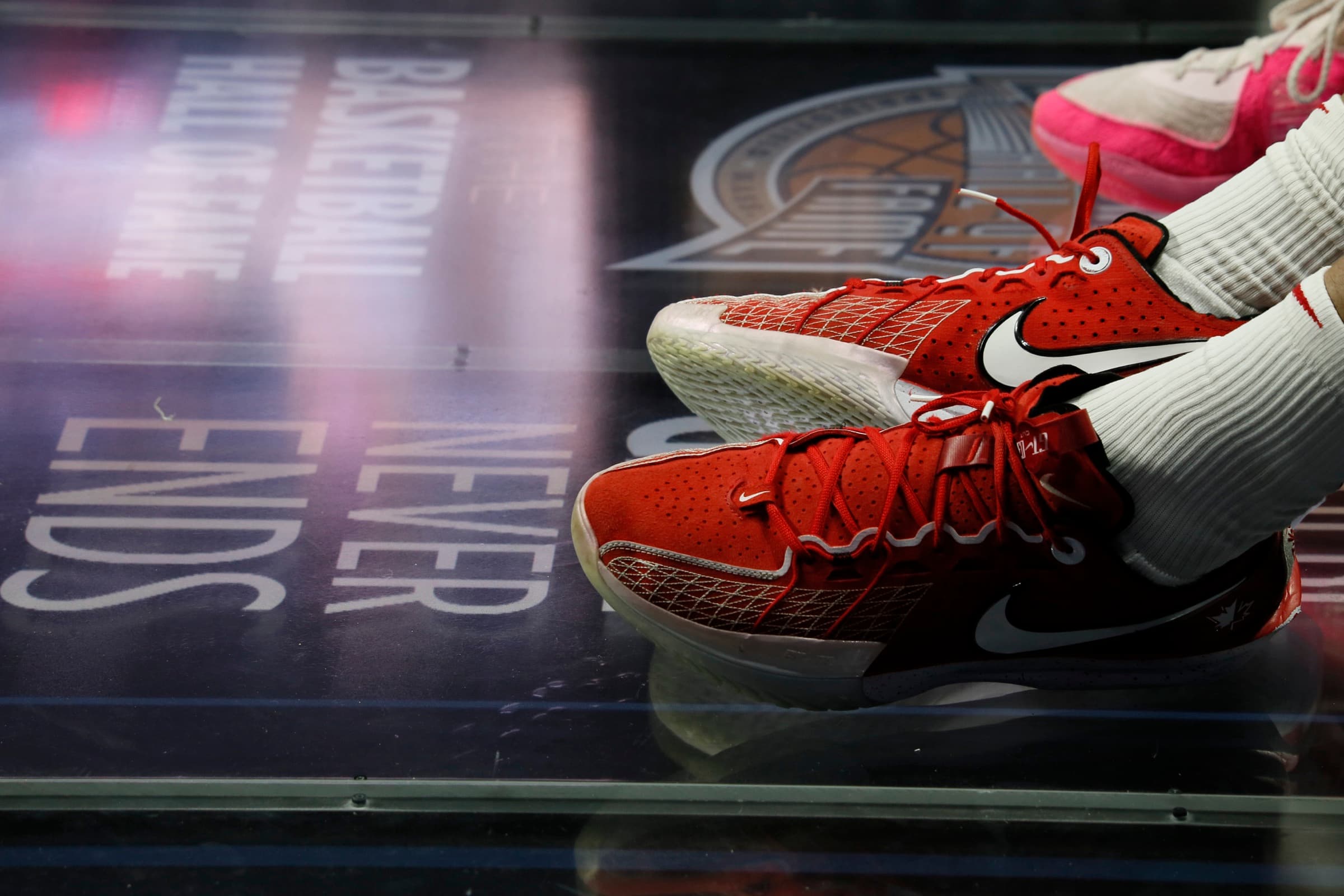 A player's red basketball shoes resting on the glass Basketball Hall of Fame floor