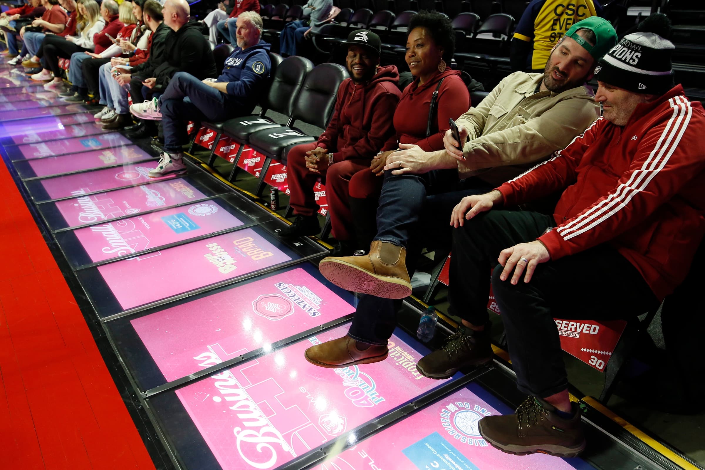 Fans in courtside seats with their feet above a row of pink Courtside floor display panels