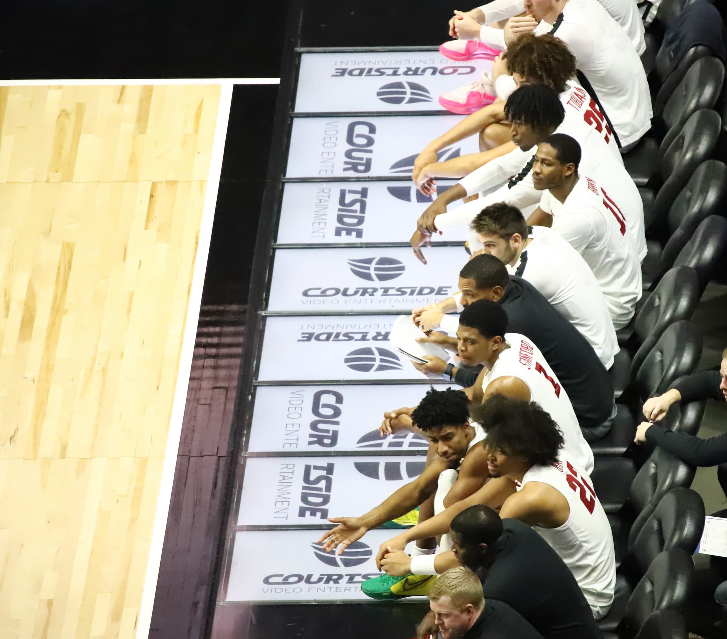 Players on the team bench lean over a row of Courtside display panels along the sideline