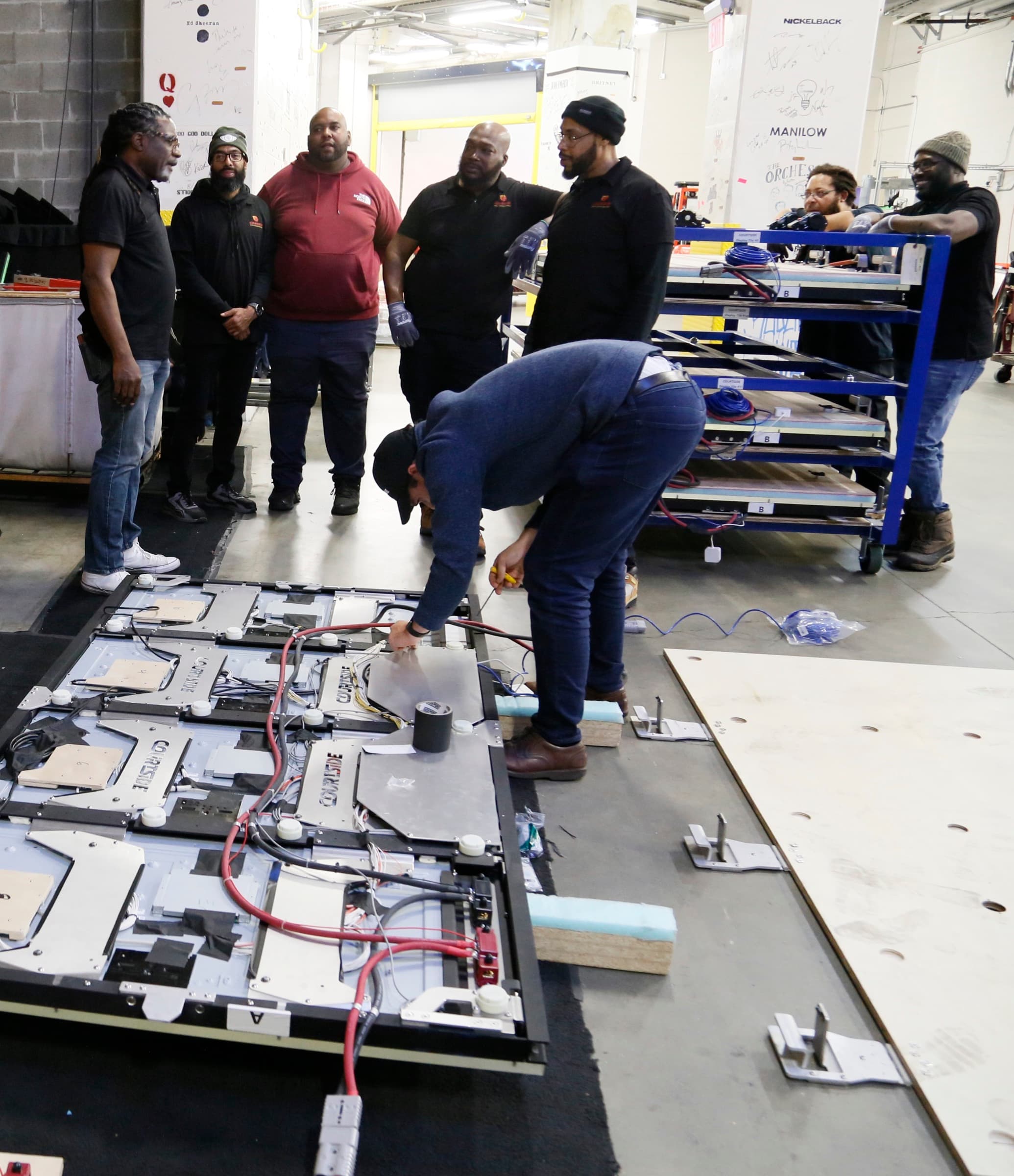Courtside crew gathered around a technician wiring an LED floor panel on the North Philadelphia production floor